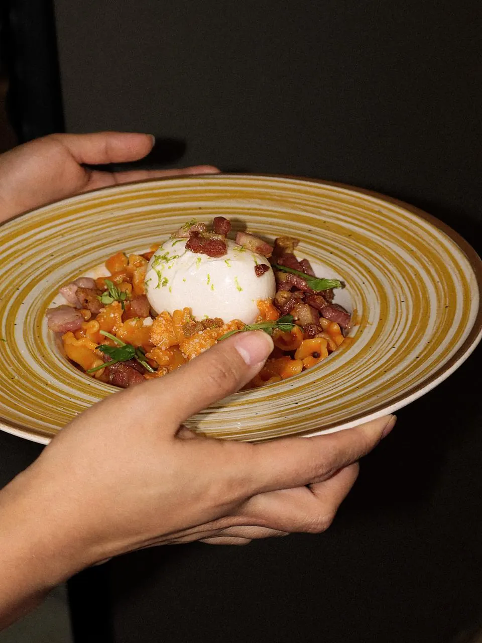 Assiette de pâtes fraîches à la tomate, pancetta et burrata, tenue à deux mains