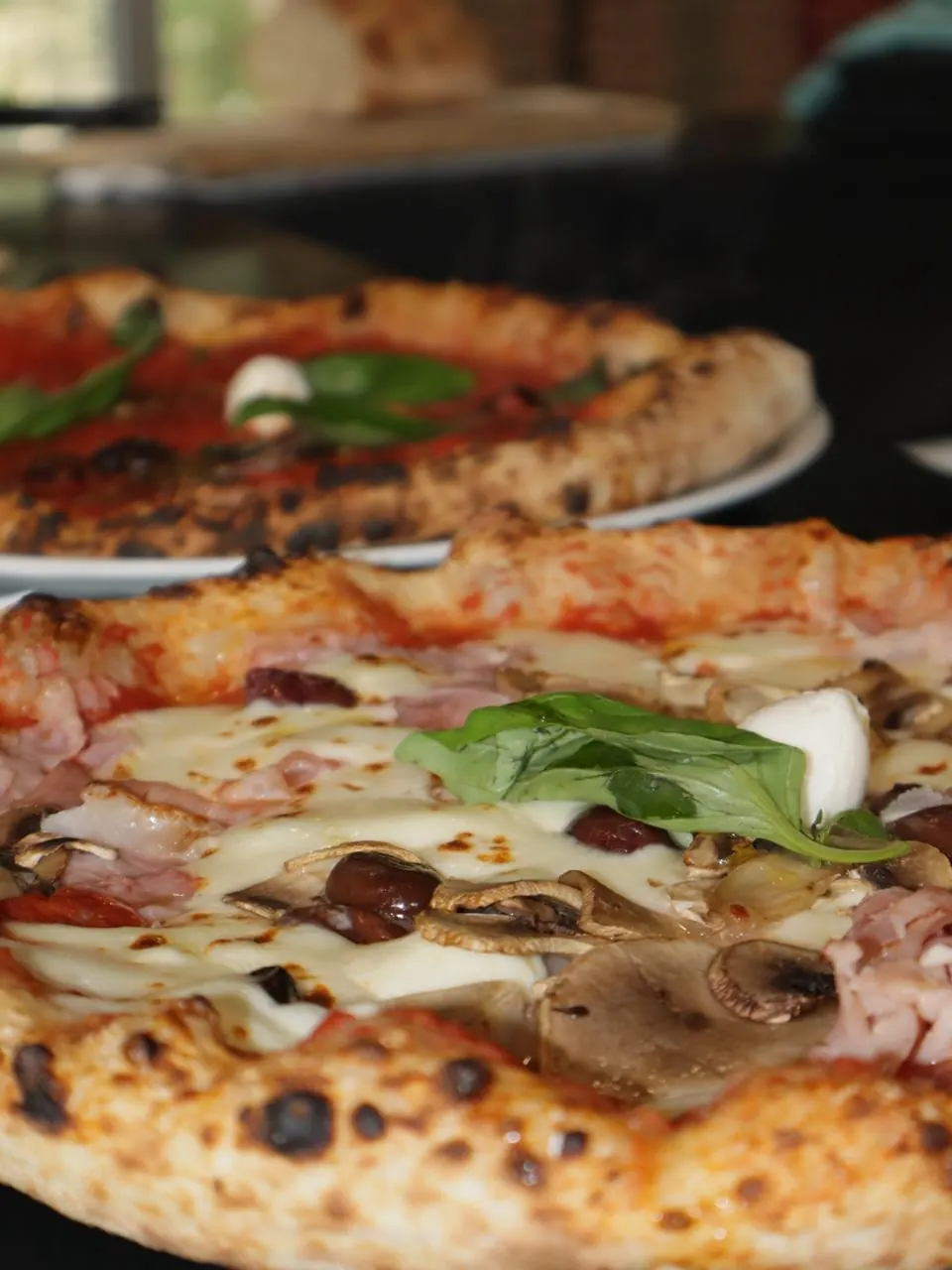 Deux pizzas napolitaines au cornicione léopardé : jambon, champignons, olives, mozzarella et basilic